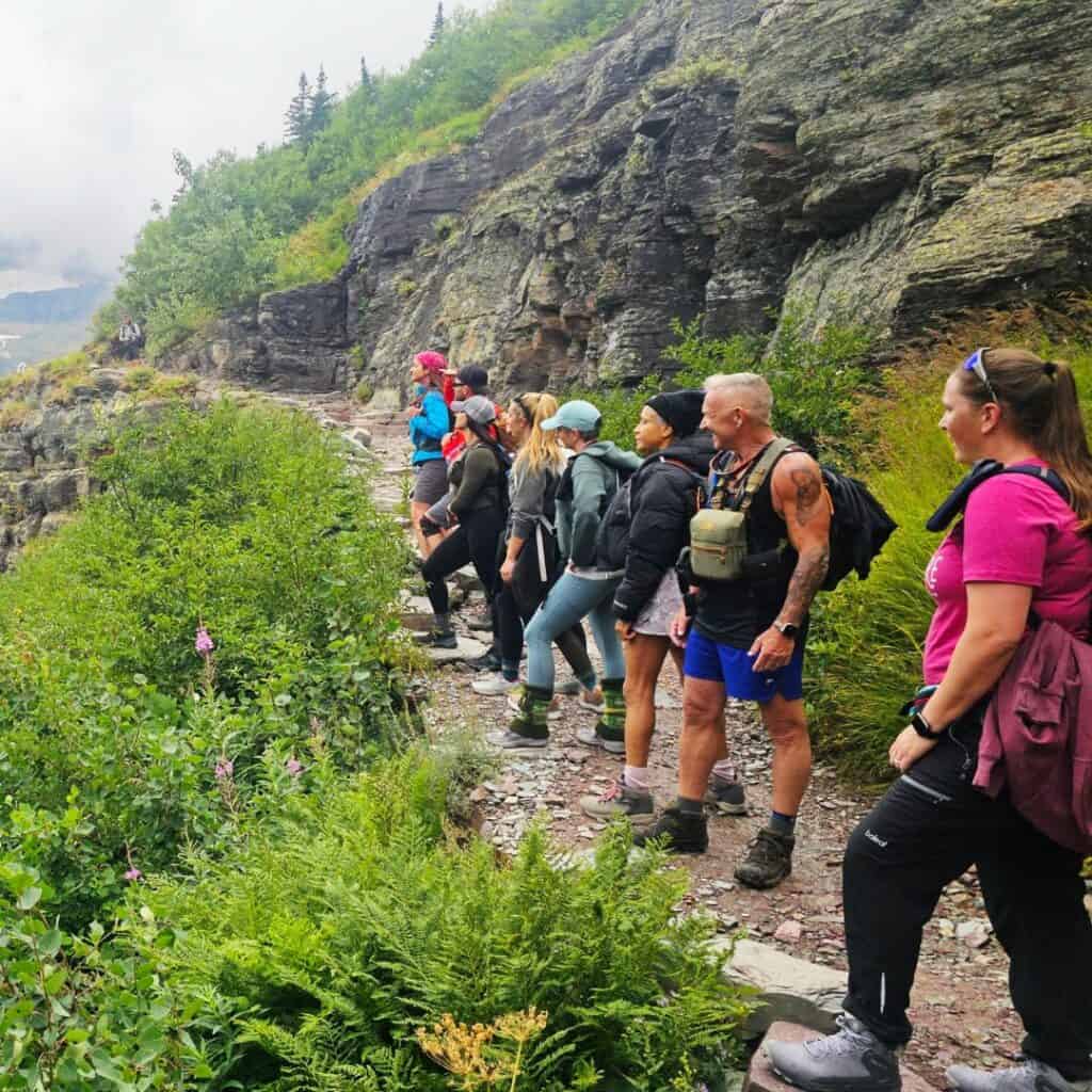 Hiking group walking along a mountain trail surrounded by lush greenery and rocky cliffs.