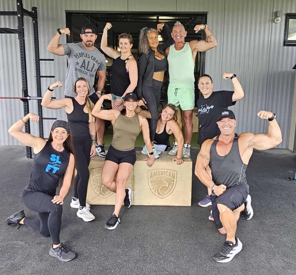 Group of diverse people flexing muscles after workout at Soulfit Retreat gym.