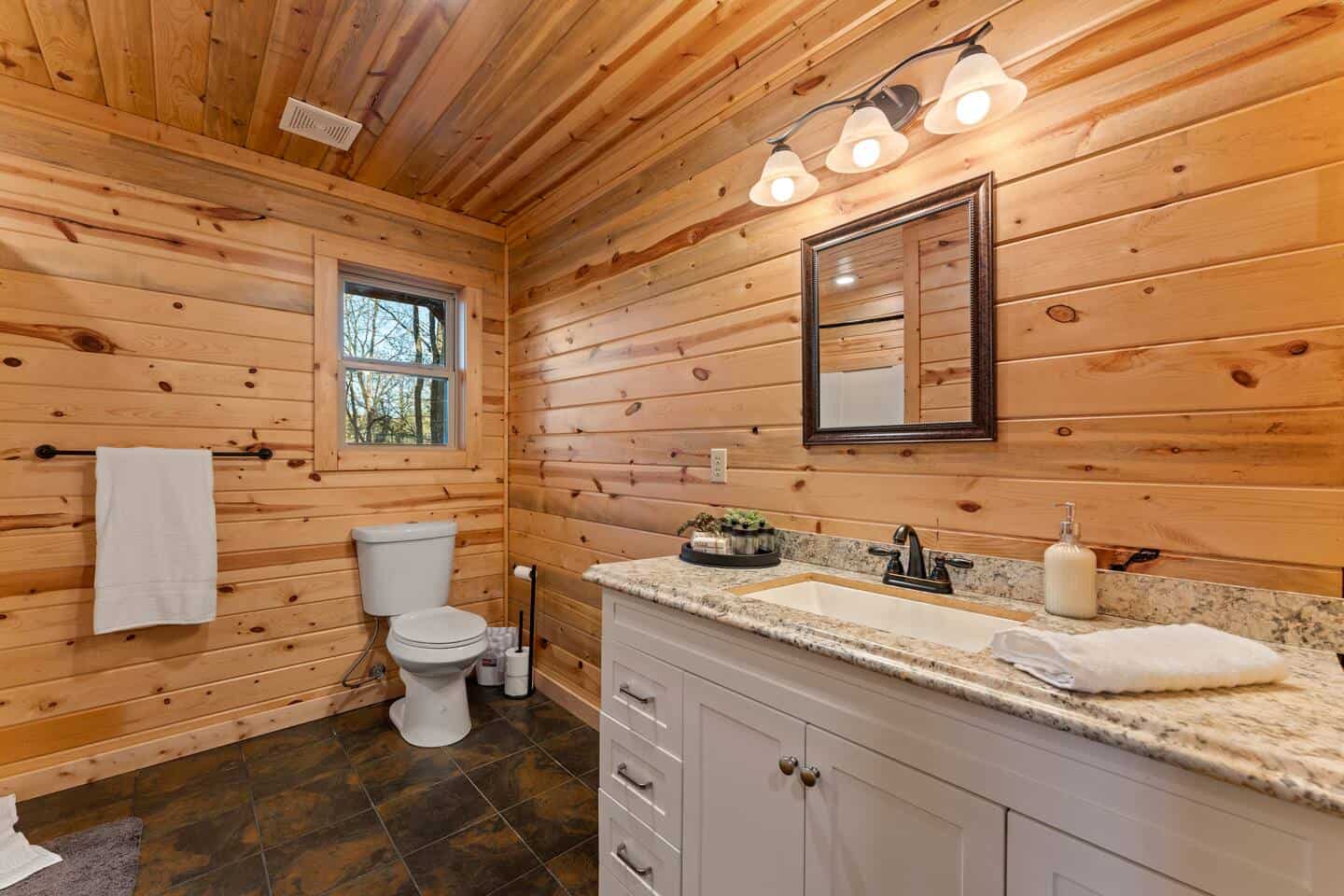 Bathroom in a cozy wooden cabin with a white vanity, granite countertop, and natural wood walls.