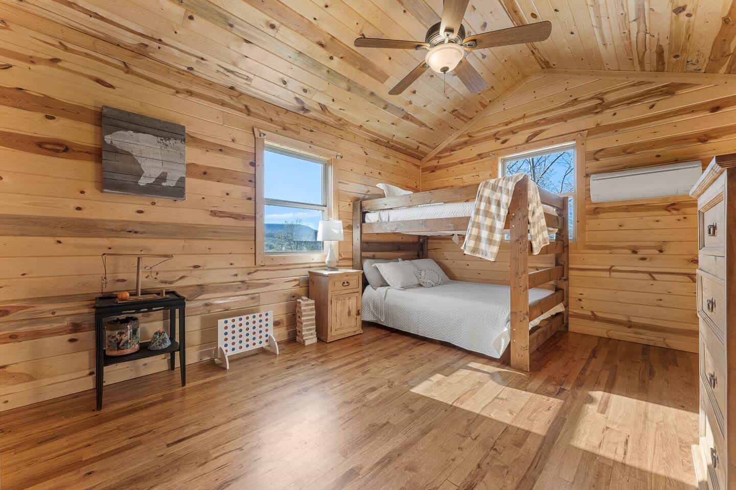 Warm wooden cabin bedroom with bunk beds, windows, and natural light.