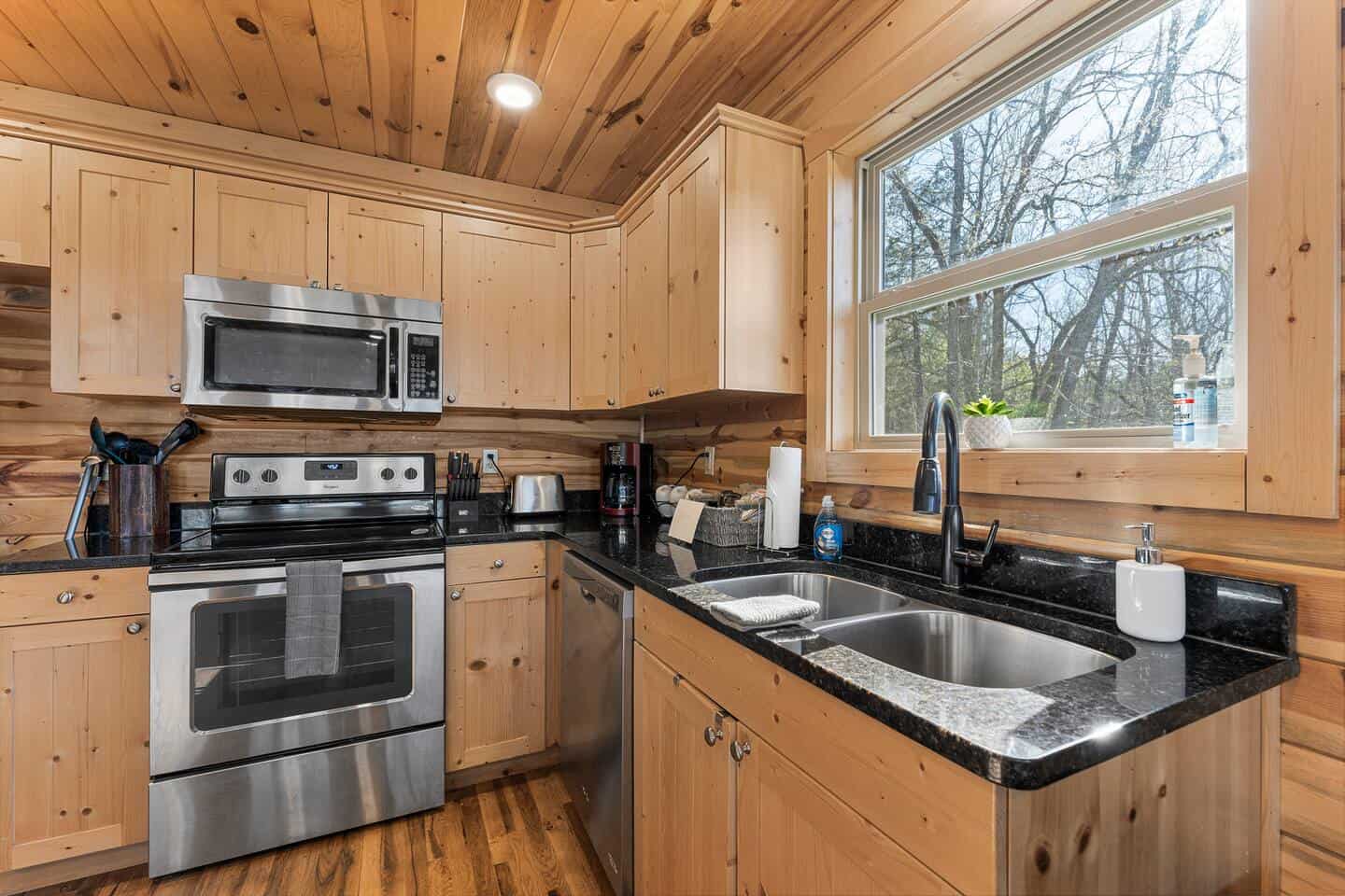 Wooden kitchen featuring stainless steel stove, microwave, and black granite countertops with a larg.