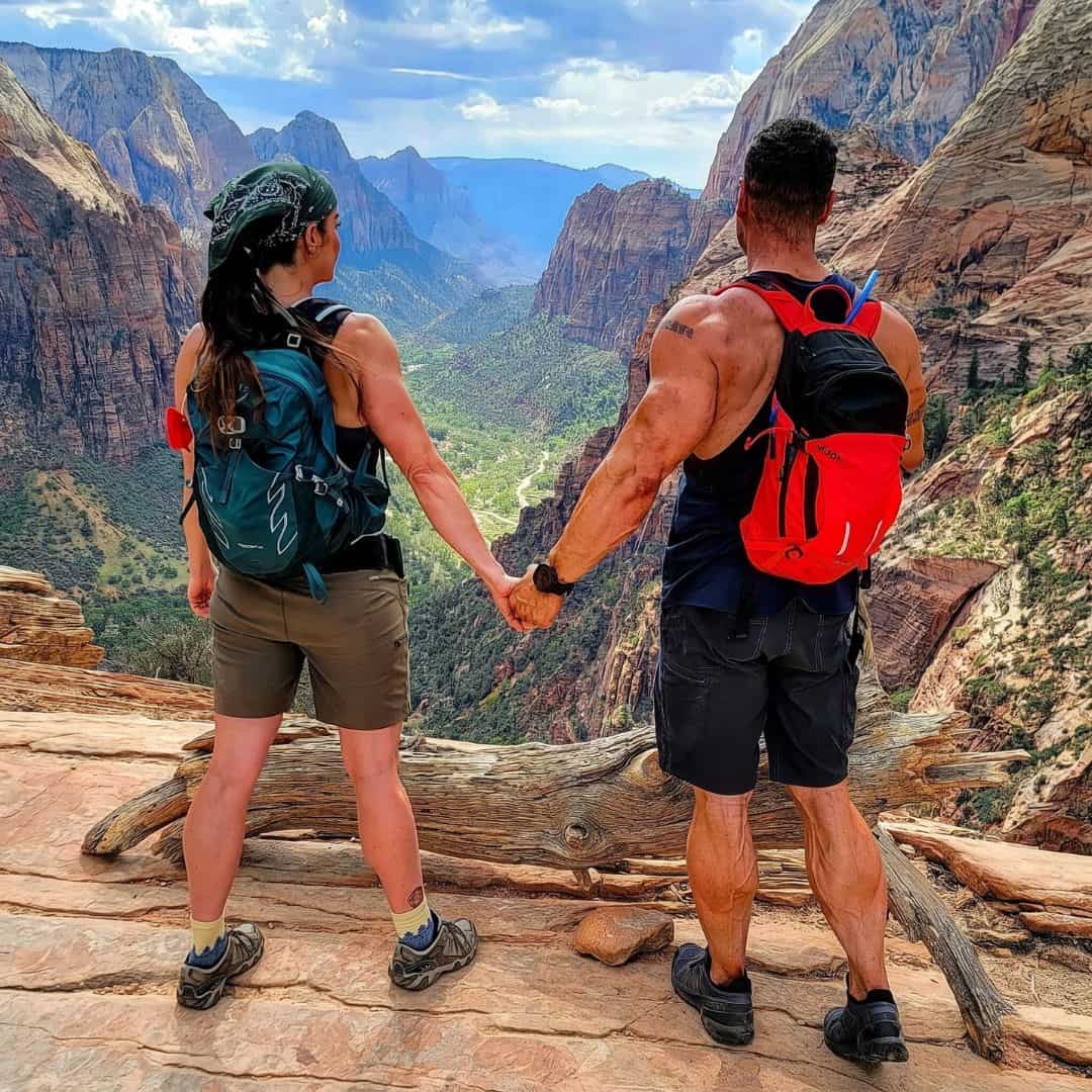 Couple holding hands on a hiking trail with canyon views in the background.